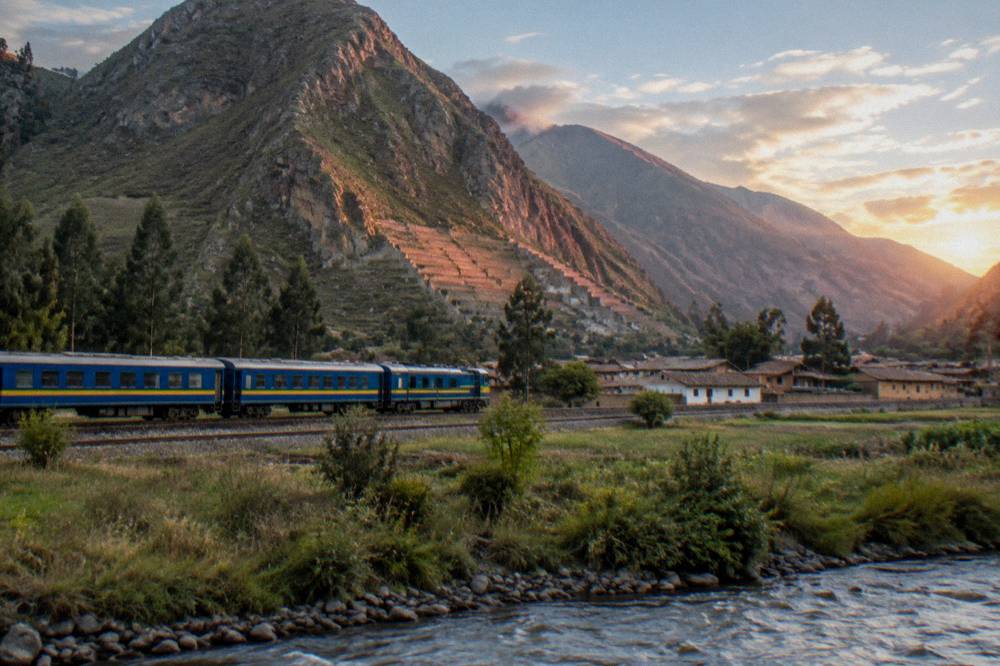 A blue and yellow passenger train crossing open altiplano grassland on a straight rail line