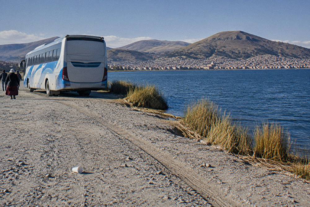 A tour bus beside the deep blue water of Lake Titicaca near Puno under a wide open sky