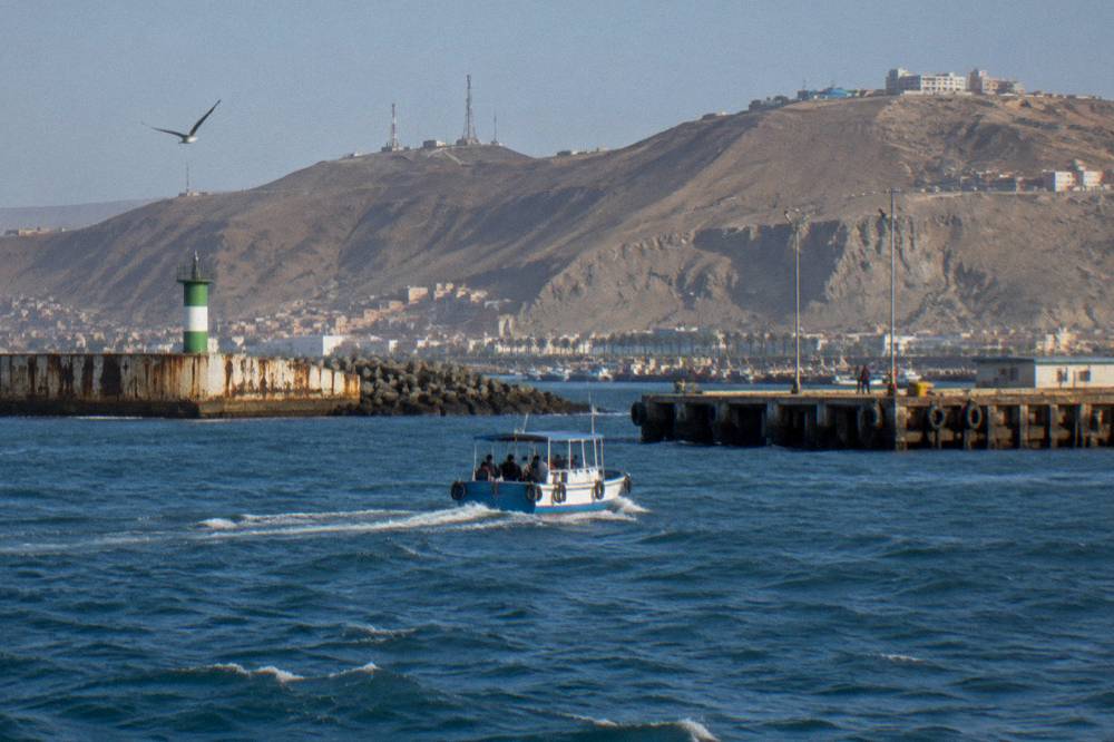 A small passenger ferry crossing a strait of blue water with dry hills rising on both sides